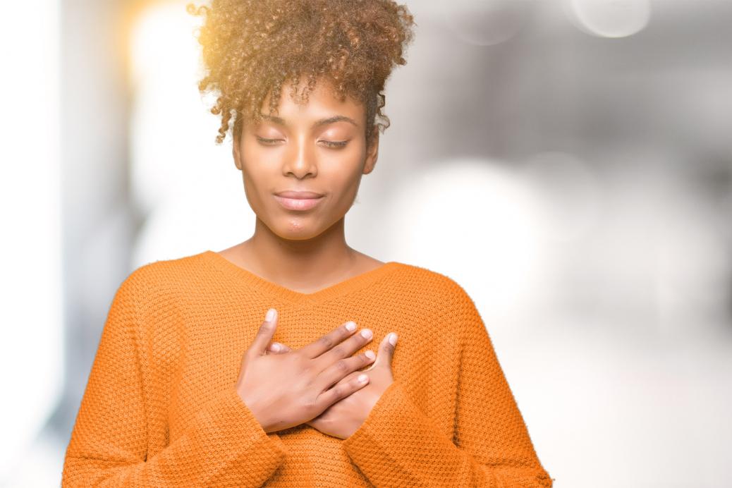 Une femme afro-américaine souriant, les mains sur la poitrine, les yeux fermés et un geste de reconnaissance sur le visage.