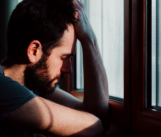 Un homme avec la tête en main appuyer sur le rebord de fenêtre