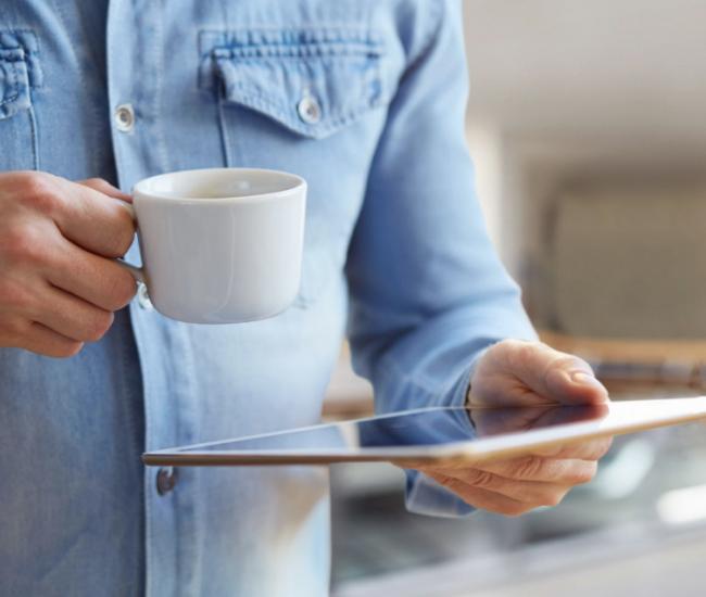 Homme avec un café qui lit sur sa tablette